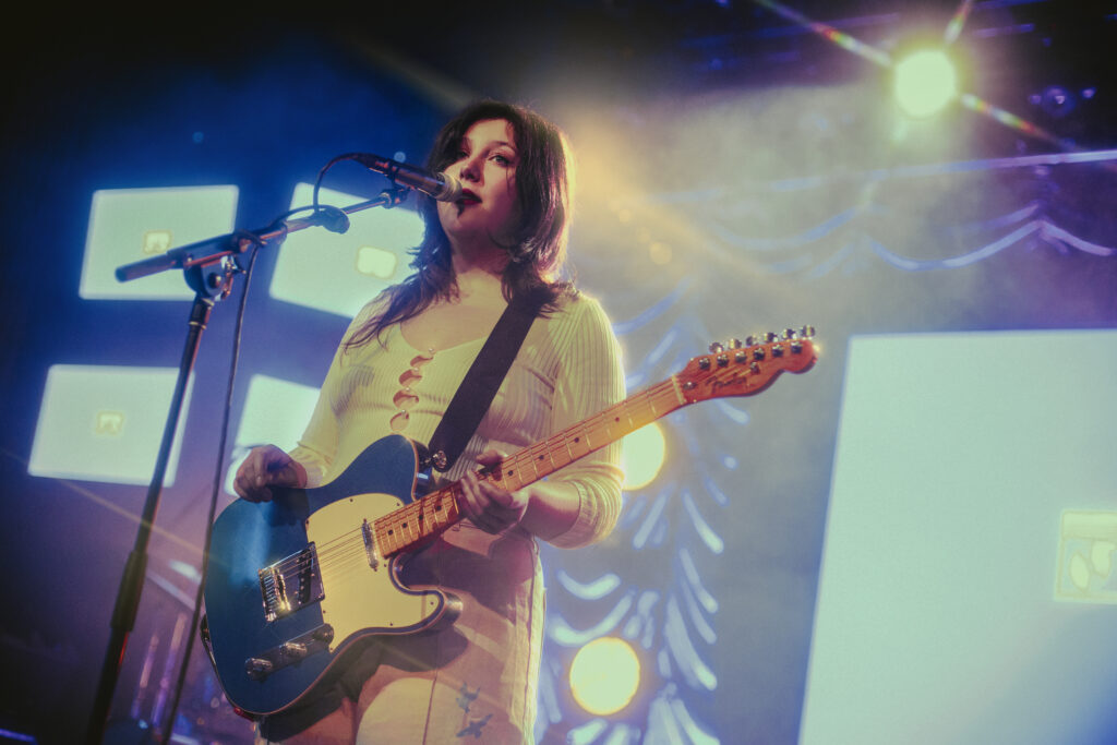Lucy Dacus shimmers under golden light as she sings while looking out to the crowd.
